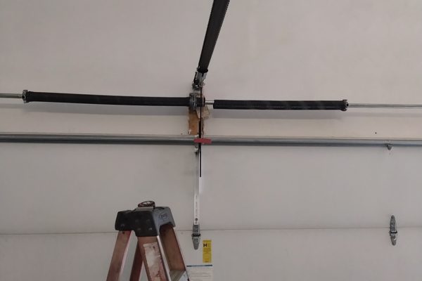 Garage door spring repair in Virginia Beach: the torsion pair on the shaft before replacement, with the opener arm and red emergency release visible