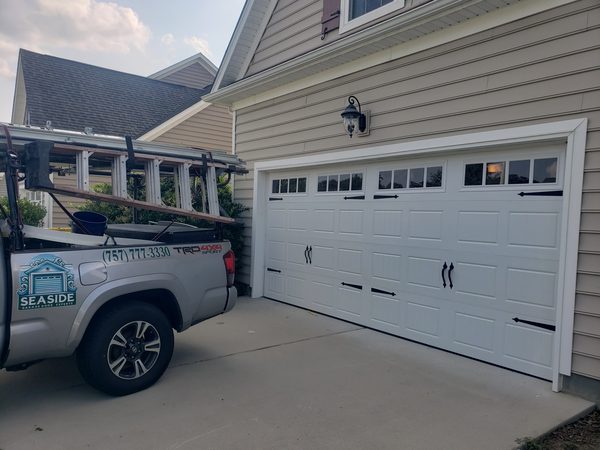 White carriage-style insulated garage door freshly installed on a Hampton Roads home, actual Seaside job with the service truck in the driveway