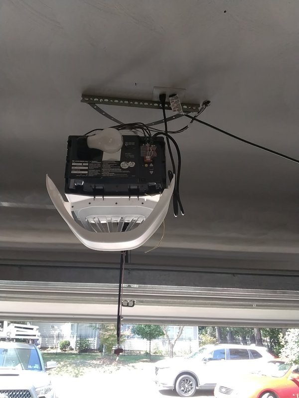 Old ceiling-mounted Chamberlain chain-drive garage door opener with exposed motor housing and wiring, before removal, in a Cape Charles, Virginia garage