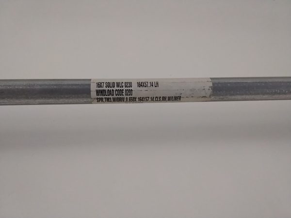 Close-up of the factory label wrapped around a Wayne Dalton TorqueMaster spring tube reading 16X7 SOLID WLC 0230, WINDLOAD CODE 0230, and SPR TM3 W/DRIV 0.650X.164X57.14 CLS RH W/LINER