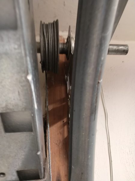 Close-up of a garage door cable drum with slack cable beside the vertical track