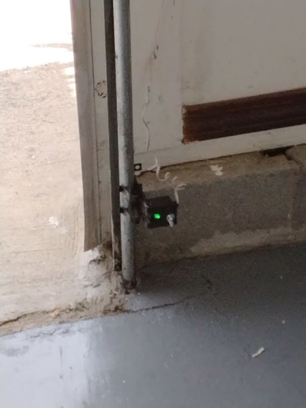 New garage door safety sensor with its green light on, mounted at the bottom of the track in Hampton, VA, July 2026