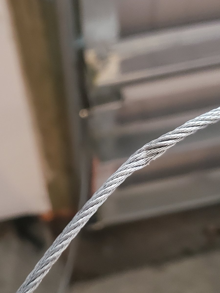 Frayed garage door lift cable wrapping around a cable drum, an early post-storm warning sign